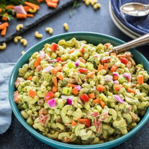 vegan macaroni salad served in a blue bowl with some plated and chopped veggies in the background