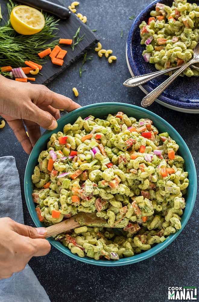 pair of hands mixing vegan macaroni salad with a spatula