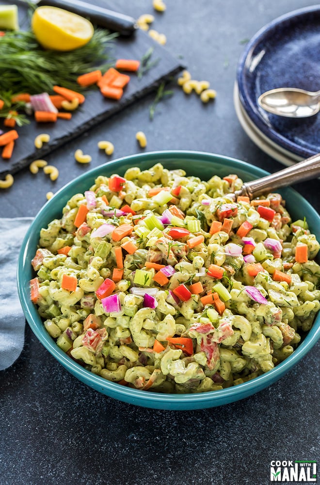 vegan macaroni salad served in a blue bowl with some plated and chopped veggies in the background