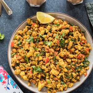 tofu scramble in a round plate with a glass of chai in the background