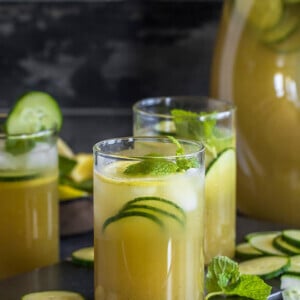 three glasses of a cucumber lemonade with a pitcher in the background