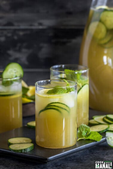 three glasses of a cucumber lemonade with a pitcher in the background