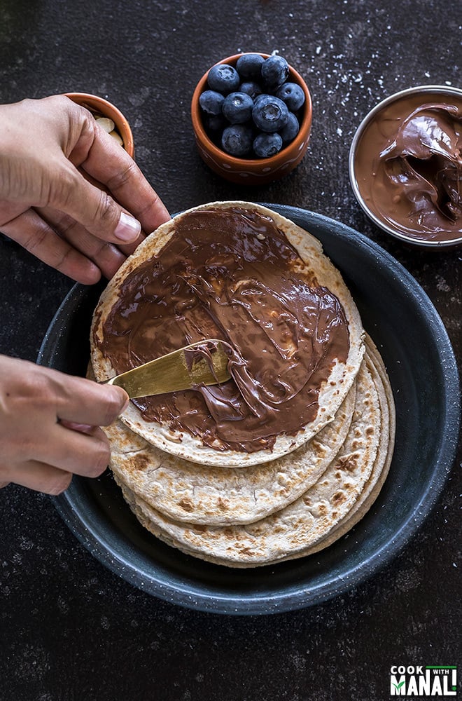 a pair of hands applying nutella on rotis