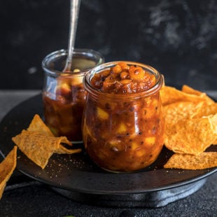 peach chutney in a small glass jar with chips on the side