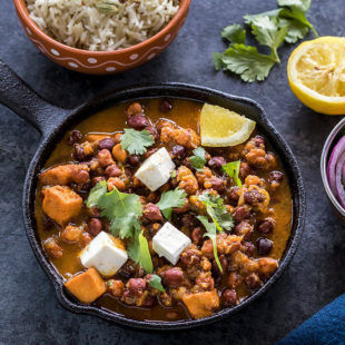 kala chana or black chickpeas curry served in a small cast iron skillet with a bowl of rice in the background and a squeezed lemon and some cilantro on the side