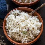 overhead shot of jeera rice served in a clay bowl with a spoon on the side