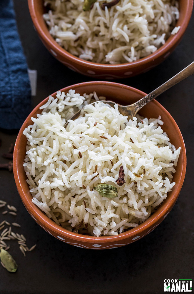 overhead shot of jeera rice served in a clay bowl with a spoon on the side