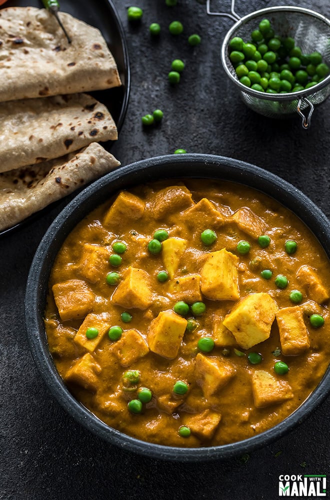 matar paneer in a black round bowl with rotis in the background