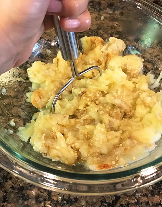 roasted eggplant being mashed in a glass bowl