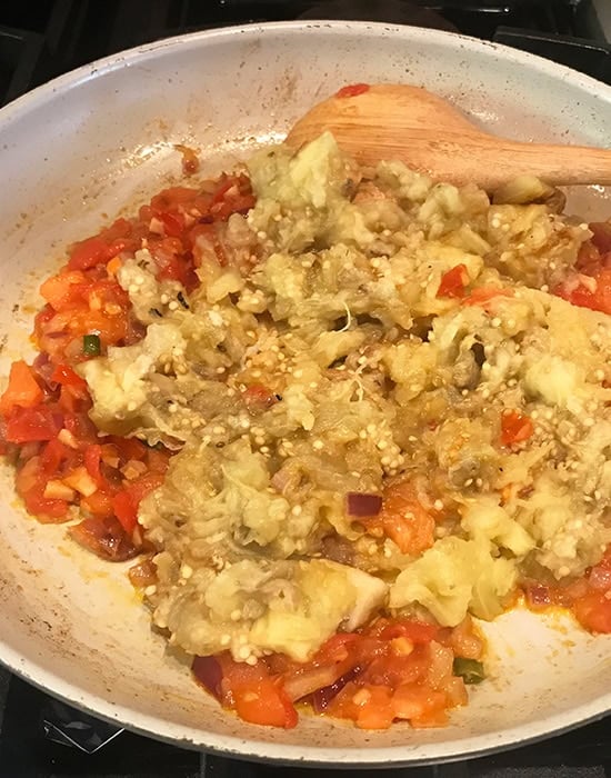 mashed eggplant added to onion tomato masala in a pan