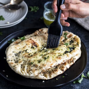 garlic naan being brushed with butter with a black pastry brush