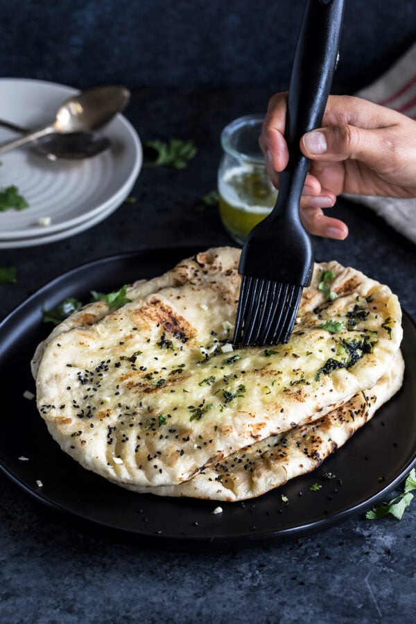 garlic naan being brushed with butter with a black pastry brush