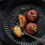 3 pieces of gulab jamun, with one being cut in half, garnished with pistachios served on a round black plate