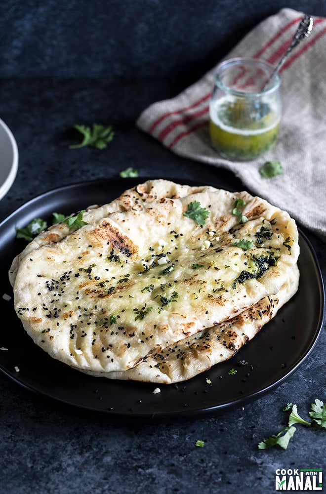 homemade garlic naan arranged in a black plate with a piece of fabric in the background