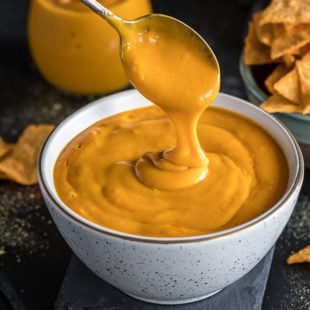 vegan cheese sauce being poured with a spoon in a white bowl