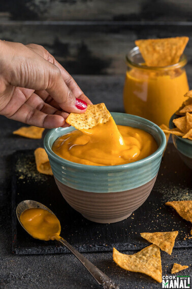a hand dipping chips into a bowl of vegan cheese sauce made in the instant pot