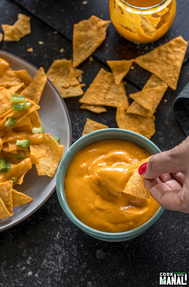 a hand dipping chips into a bowl of vegan cheese sauce made in the instant pot
