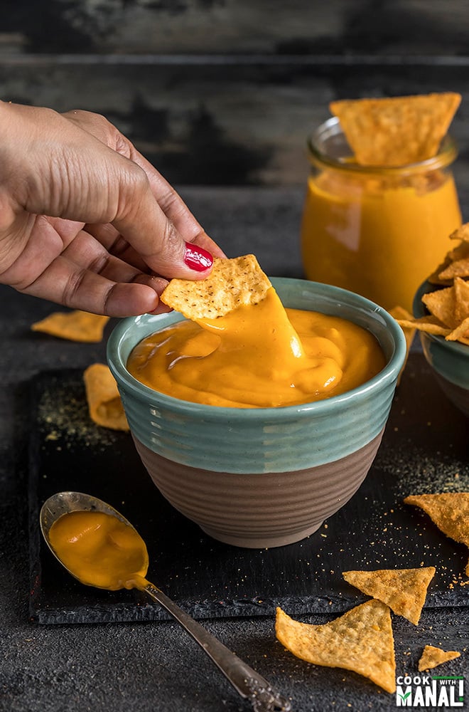 a hand dipping chips into a bowl of vegan cheese sauce made in the instant pot