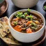 vegan lentil soup in a white bowl with bread on the side