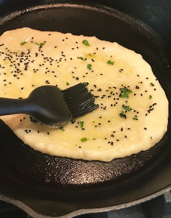 brushing naan with butter on a skillet