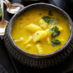 dahi aloo served in a antique copper pot with spoons in the background