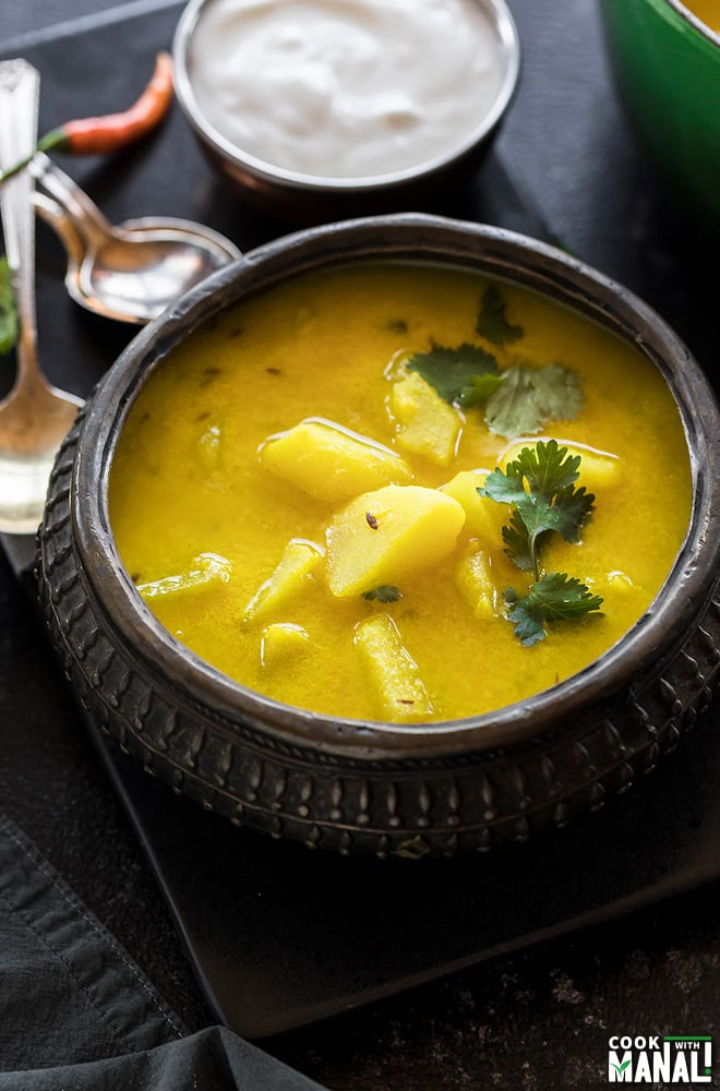 dahi aloo served in a antique copper pot with spoons in the background