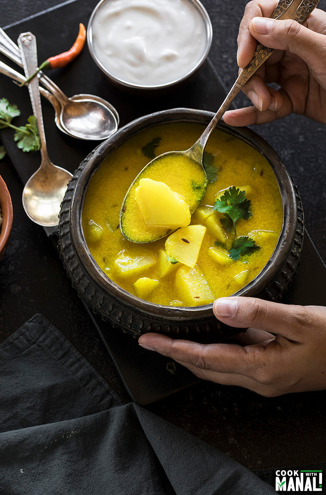 dahi aloo is a antique copper pot with a hand taking out some of the curry with a spoon