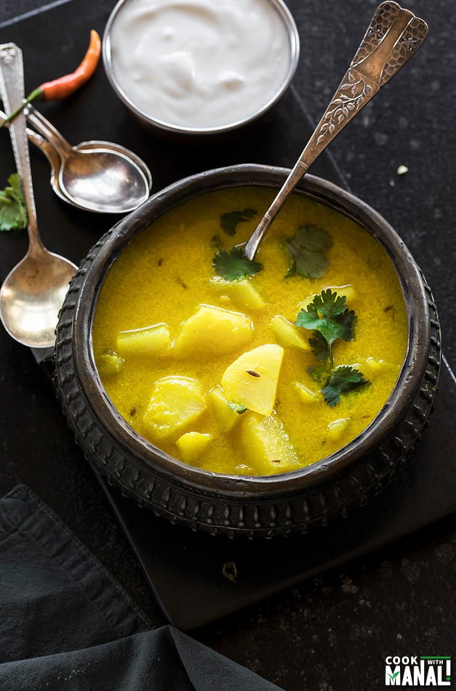 dahi aloo served in a antique copper pot with spoons in the background