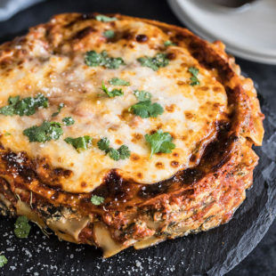 spinach mushroom lasagna on a round black serving board with a napkin and plates in the background