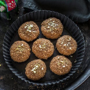seven pieces of mathura peda in a black rimmed plate with a grey color kitchen towel on the side
