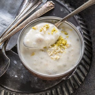 a spoon dipped in a bowl of sabudana kheer with more spoons in the background
