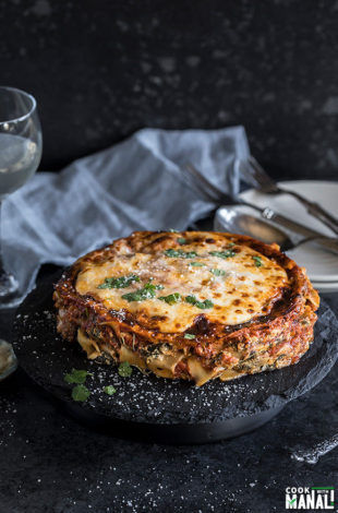 spinach mushroom lasagna on a round black serving board with a napkin and glass in the background