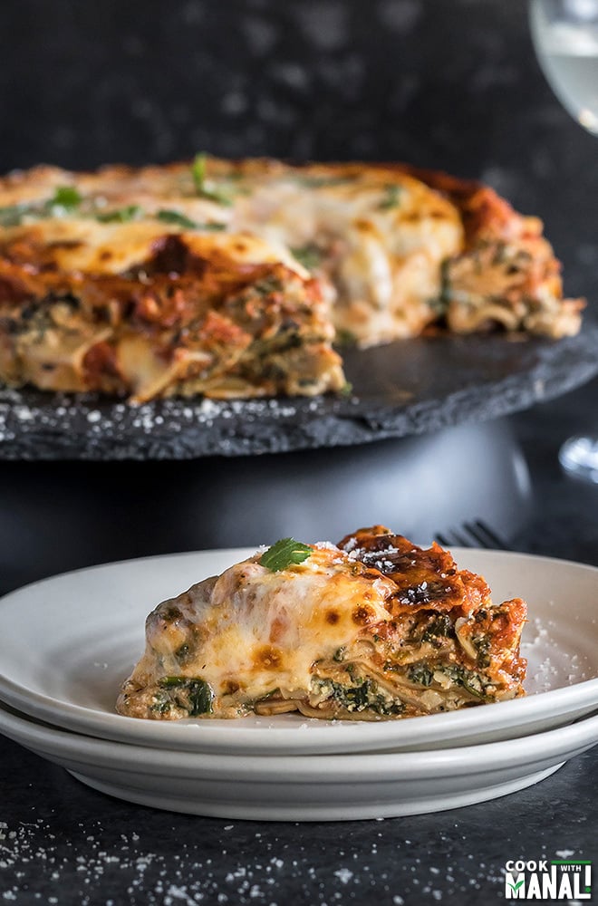 a piece of spinach mushroom lasagna served in a white plate with the whole lasagna in the background