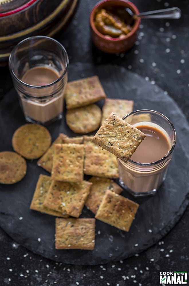 baked methi mathri placed on a round black board with 2 glasses of chai