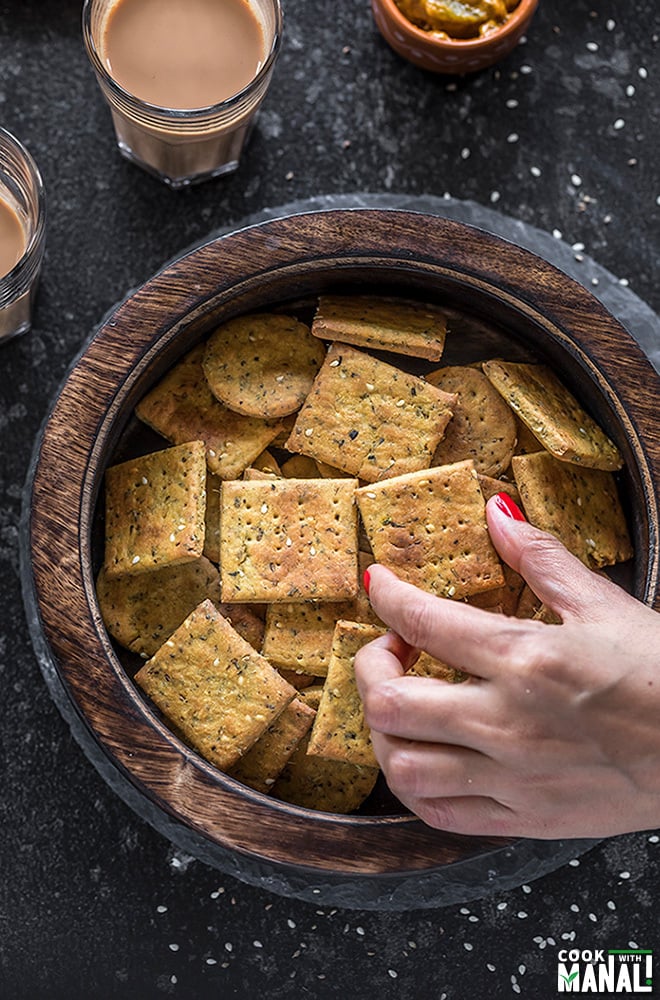 hand picking of a piece of baked methi mathri from a wooden box