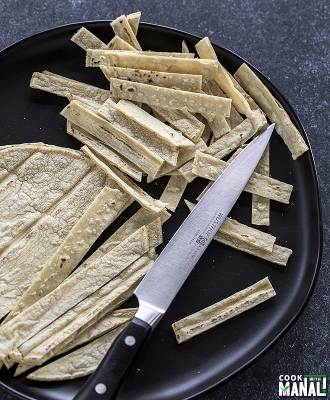 black plate with cut corn tortillas along with a knife