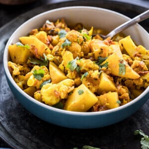 bowl of aloo gobi with a spoon and bowl of rice in the background