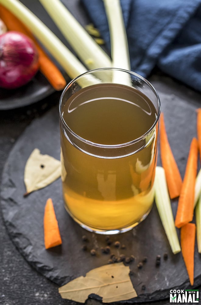 vegetable stock in a glass container with veggies on the side