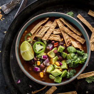 instant pot vegetarian tortilla soup in a bowl topped with tortilla strips, avocado, cilantro, lime wedge and jalapenos