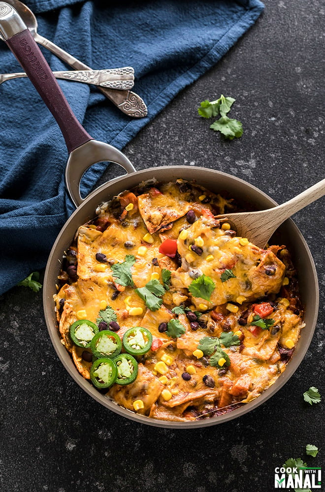 one-pot vegetarian enchiladas in a skillet with a spatula and garnished with cilantro and jalapenos