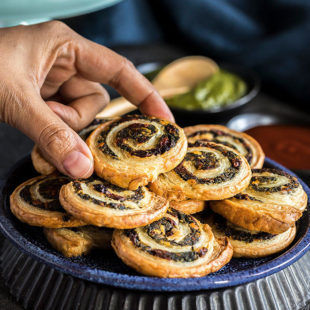 hand holding one of the puff pastry pinwheels from a blue plate