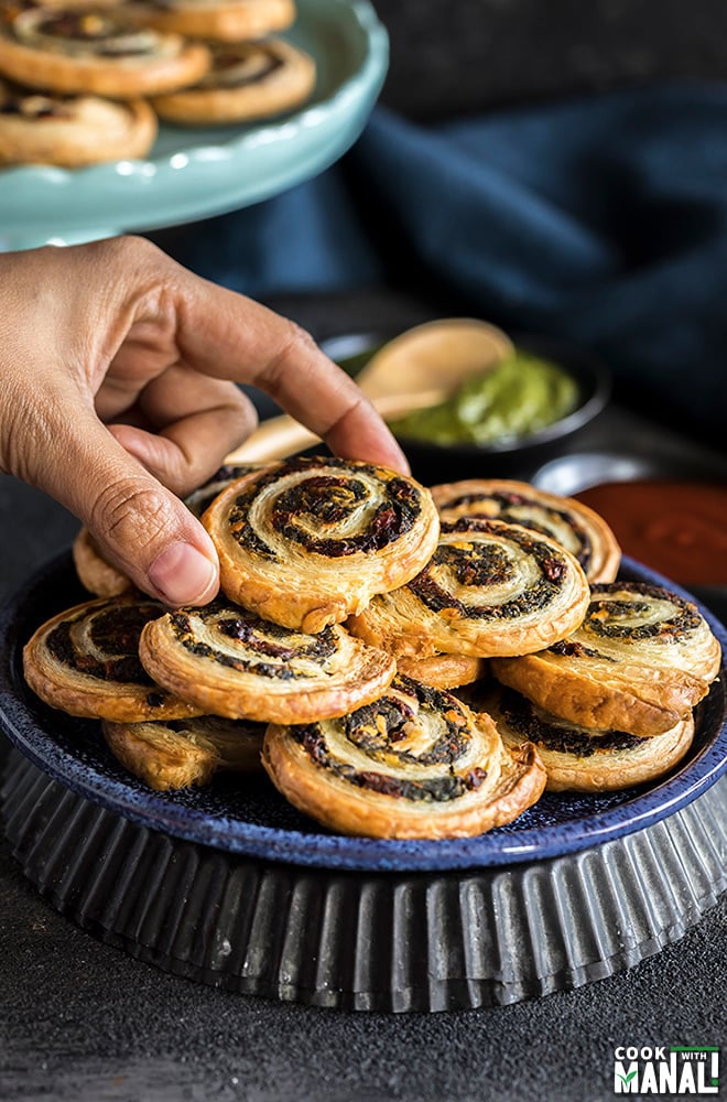 hand holding one of the puff pastry pinwheels from a blue plate