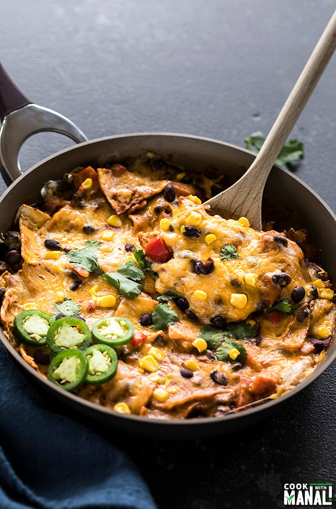 one-pot vegetarian enchiladas in a skillet with a spatula and garnished with cilantro and jalapenos