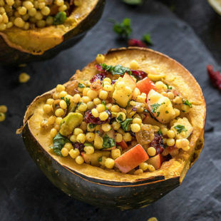 cut acorn squash stuffed with israeli couscous and garnished with fresh herbs