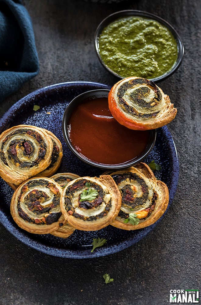 puff pastry pinwheels in a blue plate along with a black bowl of ketchup