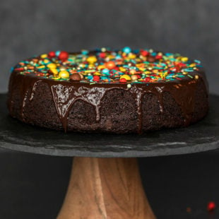 eggless chocolate cake on a black cake stand, covered with chocolate ganache and sprinkles