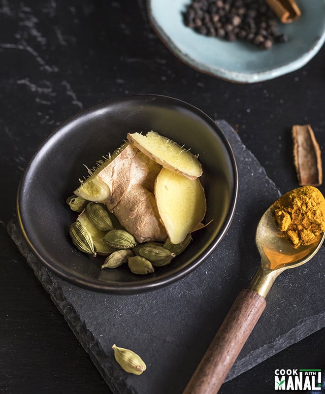 a small black bowl with ginger and cardamom and a spoon with turmeric on the side