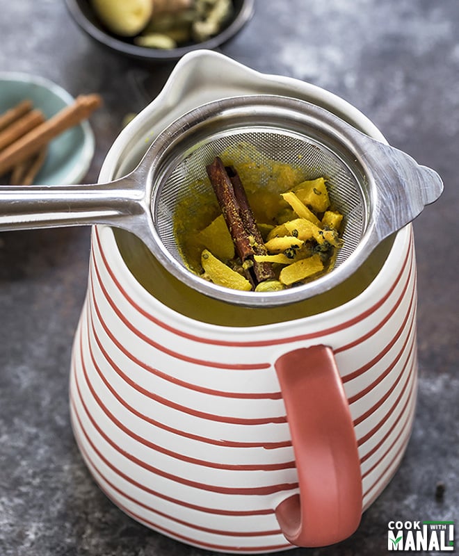 strainer with strained spices placed over a jug