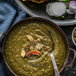 sarson ka saag served in a iron kadhai with makki roti and sliced radish and green chilies