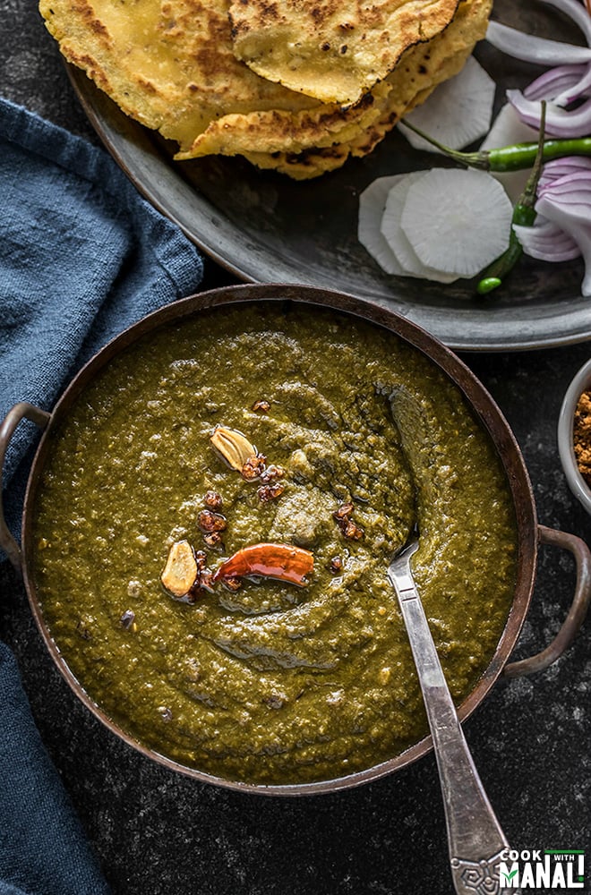 sarson ka saag served in a iron kadhai with makki roti and sliced radish and green chilies